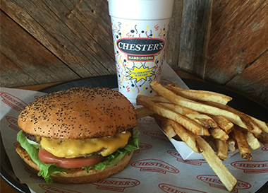 A Chester's burger with fresh-cut fries and a Chester's cup on a wood table