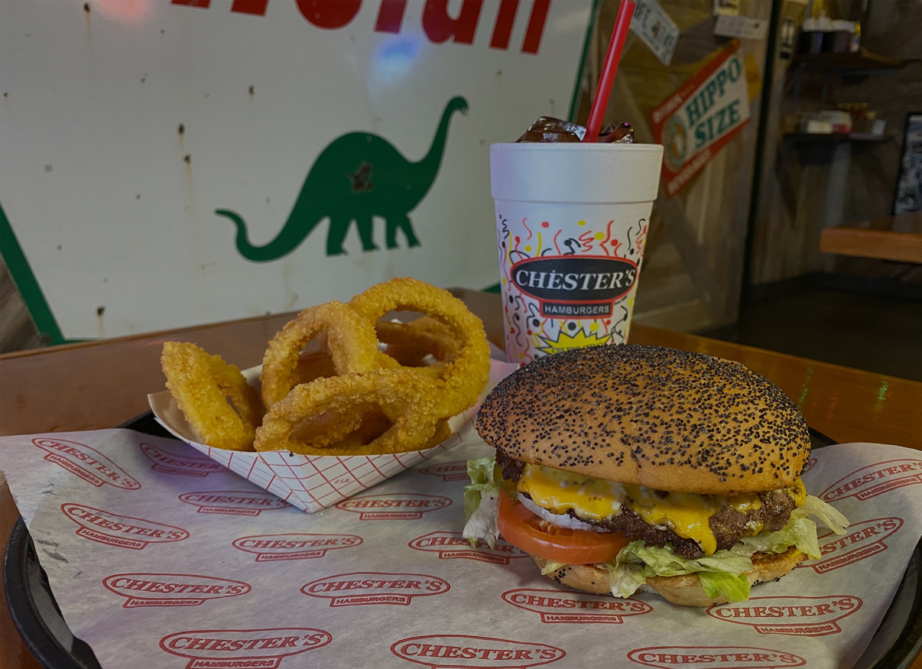 Inside Chester's Hamburgers — a tray of burger and onion rings on a wood table, with the restaurant's vintage signage on the wall behind